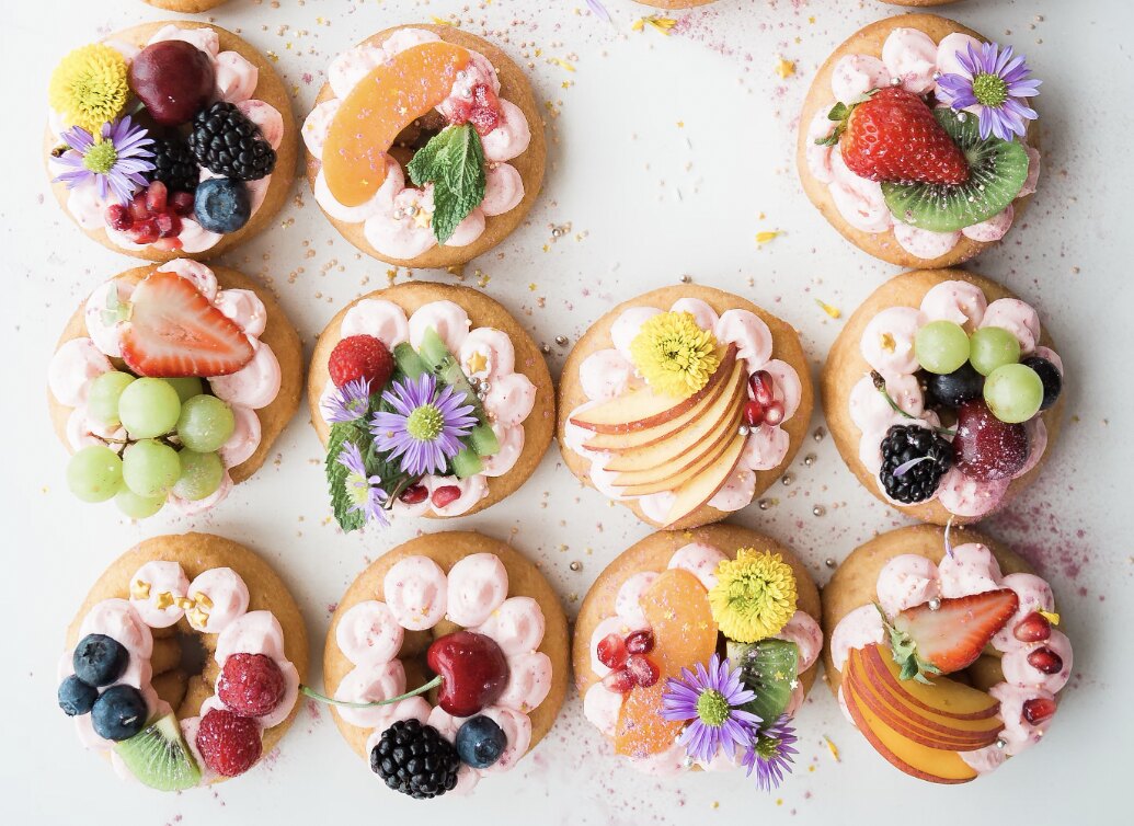 A row of doughnuts with frosting, berries, fruit and flowers as topping.